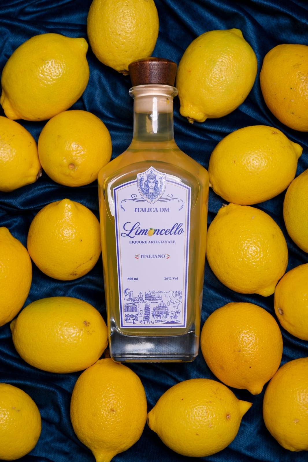 Bottle of Italica DM Limoncello surrounded by Sicilian lemons on blue velvet